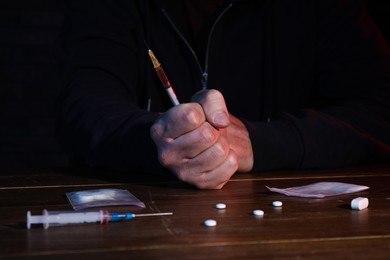Photo of Drug addicted man holding syringe at table, closeup