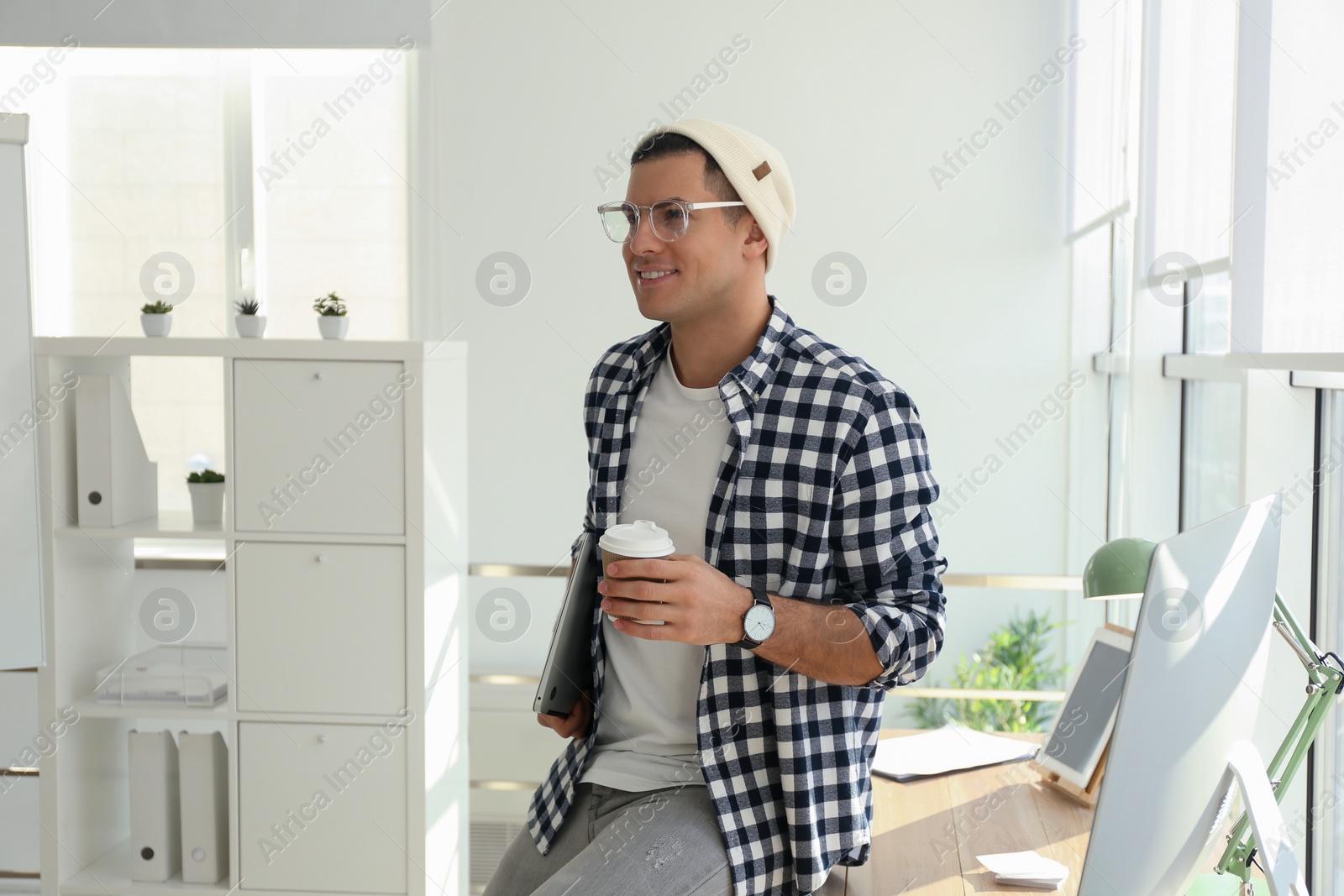 Photo of Freelancer with laptop and cup of coffee near workplace indoors