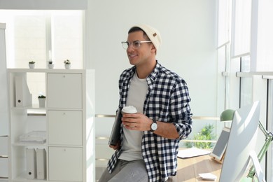 Photo of Freelancer with laptop and cup of coffee near workplace indoors