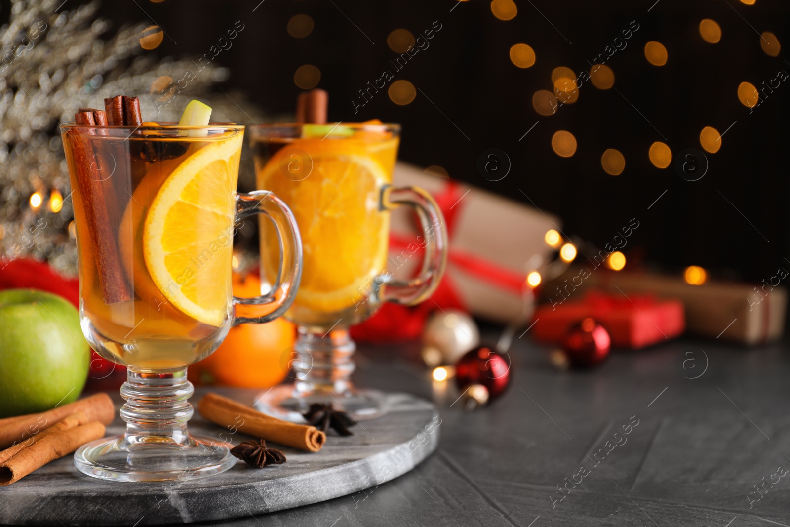 Photo of Aromatic white mulled wine on grey table against blurred lights. Space for text