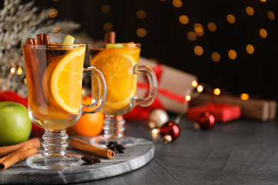 Photo of Aromatic white mulled wine on grey table against blurred lights. Space for text