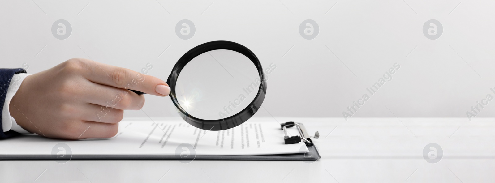 Image of Woman looking at documents through magnifier at white table, closeup. Banner design with space for text