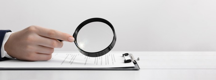 Woman looking at documents through magnifier at white table, closeup. Banner design with space for text