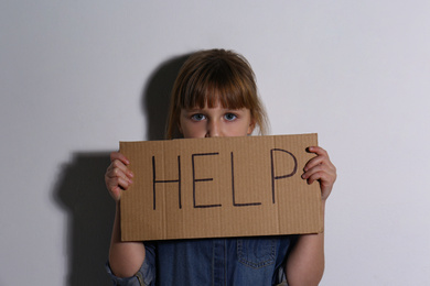 Photo of Abused little girl with sign HELP near white wall. Domestic violence concept
