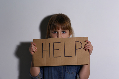 Abused little girl with sign HELP near white wall. Domestic violence concept