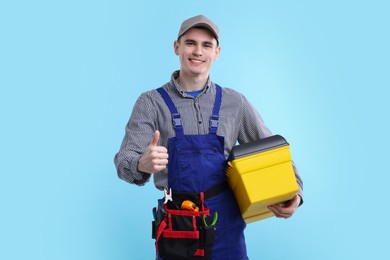 Photo of Professional repairman with tool box showing thumbs up on light blue background