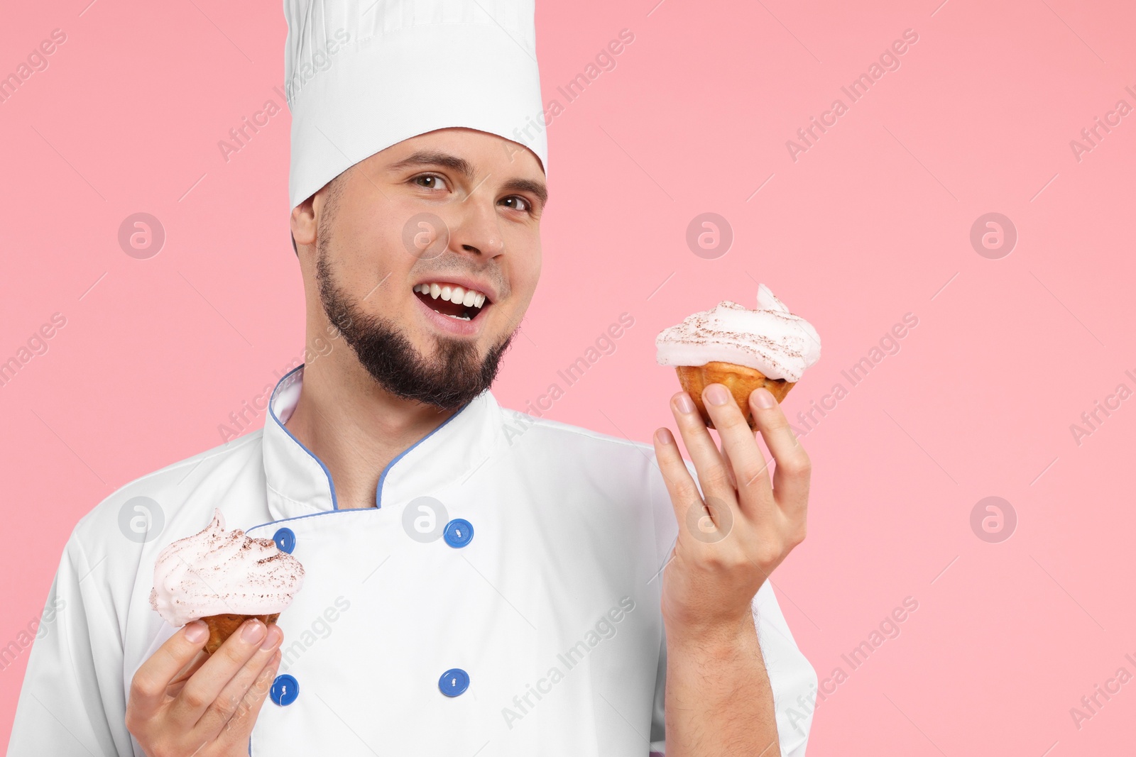 Photo of Happy professional confectioner in uniform holding delicious cupcakes on pink background