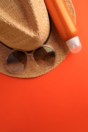 Bottle of sunscreen and beach accessories on coral background, top view. Space for text