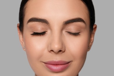 Photo of Beautiful young woman showing extended and ordinary eyelashes on grey background, closeup