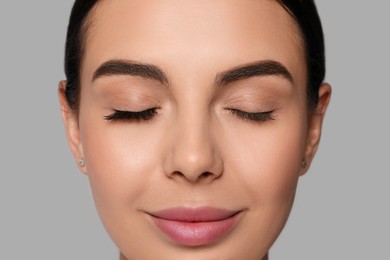 Beautiful young woman showing extended and ordinary eyelashes on grey background, closeup