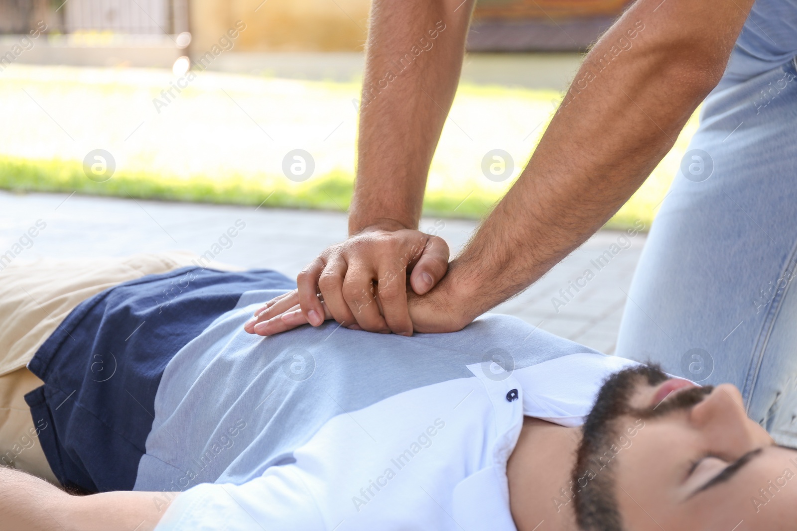 Photo of Passerby performing CPR on unconscious young man in park, closeup. First aid