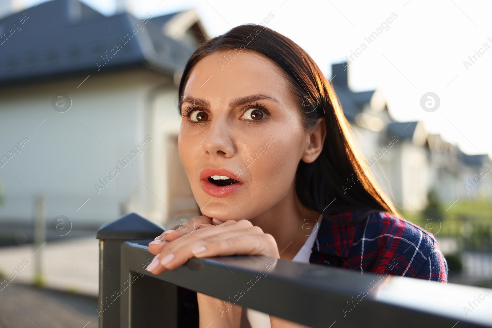 Photo of Concept of private life. Curious young woman spying on neighbours over fence outdoors