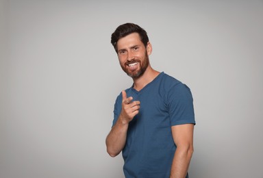 Photo of Smiling bearded man pointing forward finger on grey background. Space for text