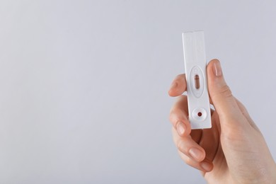 Photo of Woman holding disposable express test on light background, closeup. Space for text