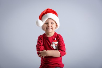 Cute little boy wearing Santa Claus hat on light grey background