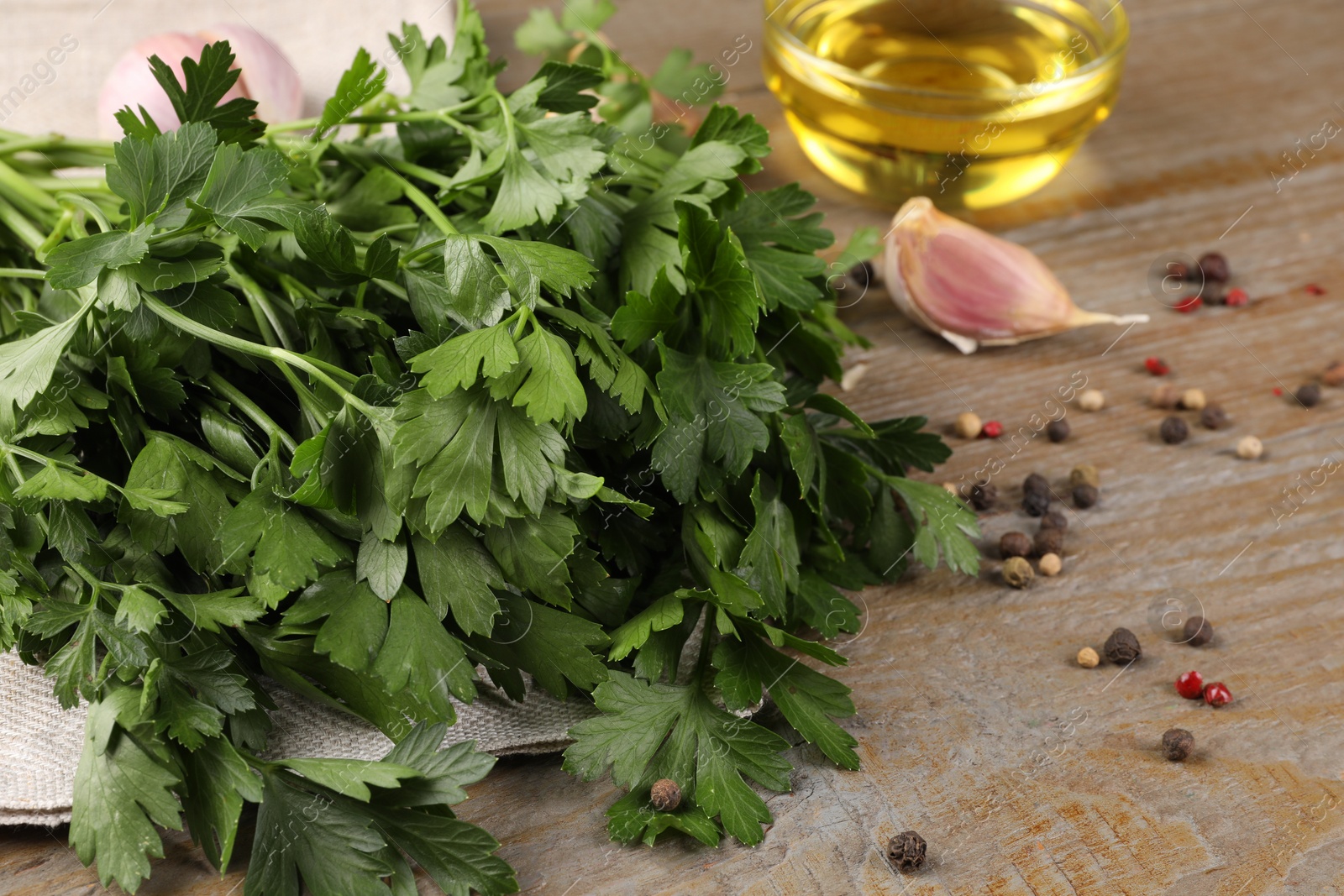 Photo of Bunch of raw parsley, oil, garlic and peppercorns on wooden table, closeup