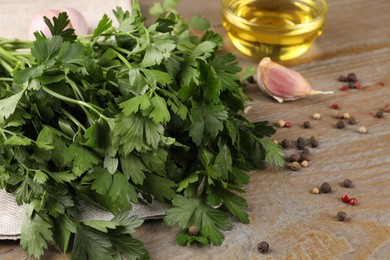 Photo of Bunch of raw parsley, oil, garlic and peppercorns on wooden table, closeup