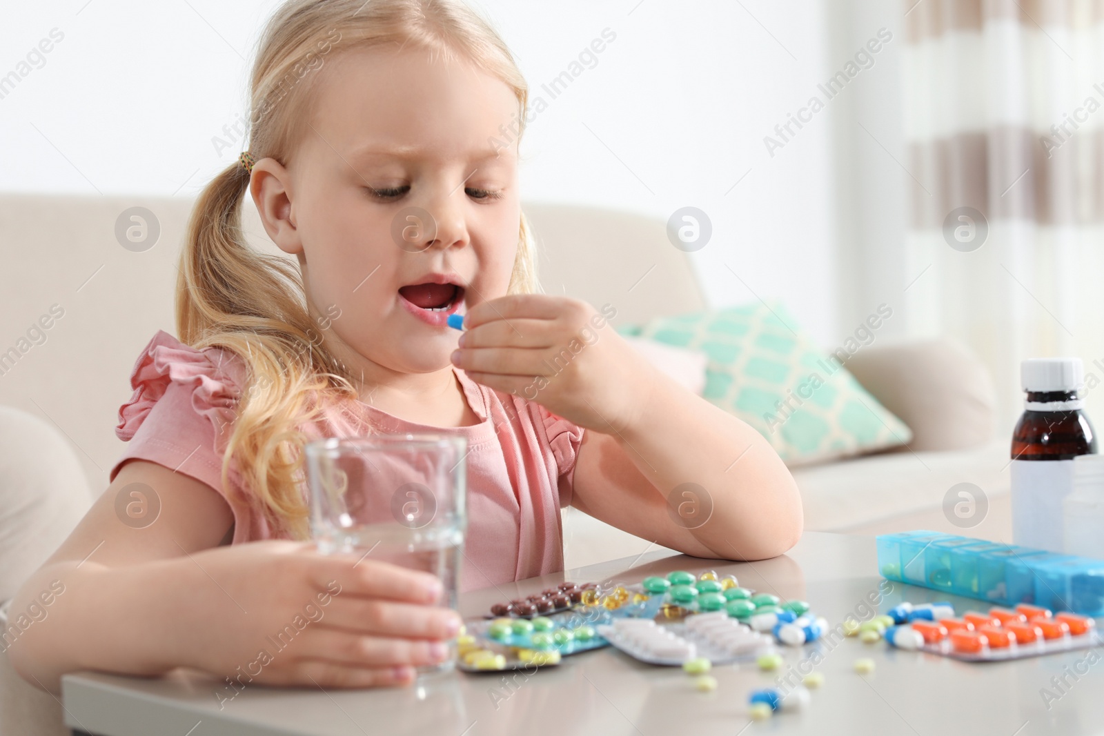 Photo of Little child taking pill at table indoors. Danger of medicament intoxication