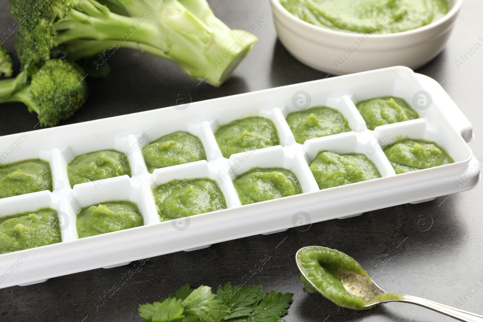 Photo of Broccoli puree in ice cube tray and ingredients on grey table, closeup. Ready for freezing