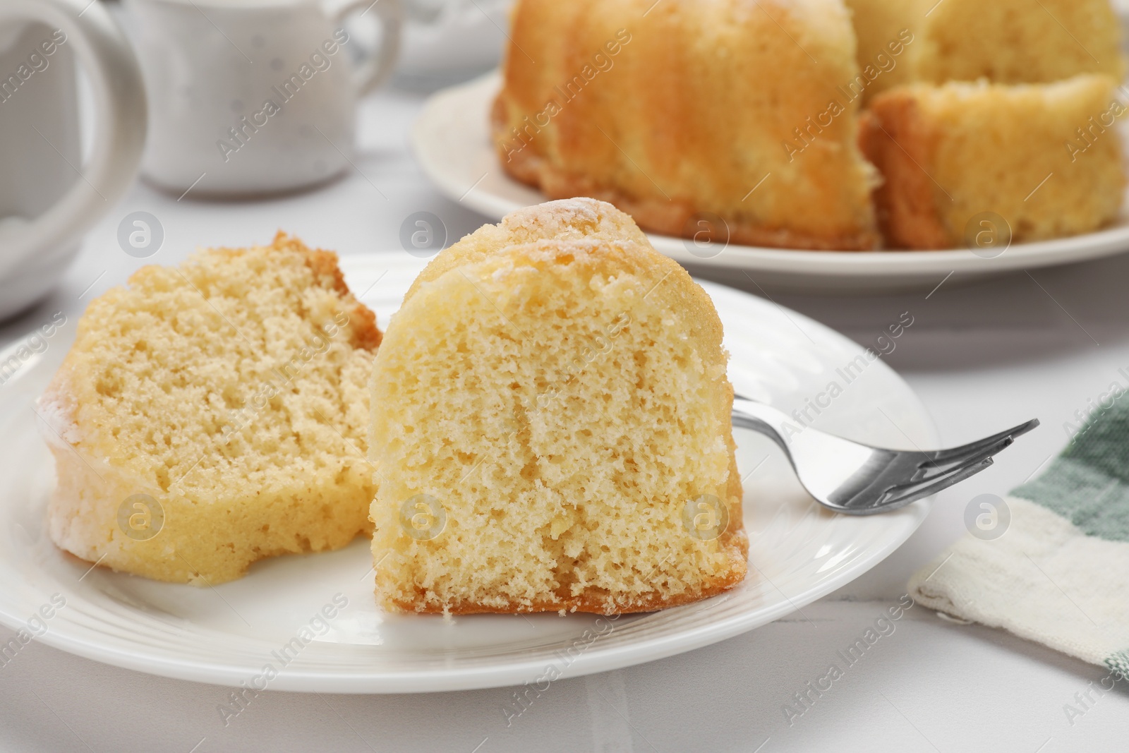 Photo of Pieces of delicious sponge cake and fork on white table, closeup