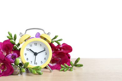 Photo of Yellow alarm clock and spring flowers on wooden table against white background, space for text. Time change