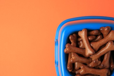 Photo of Blue bowl with bone shaped dog cookies on orange background, top view. Space for text