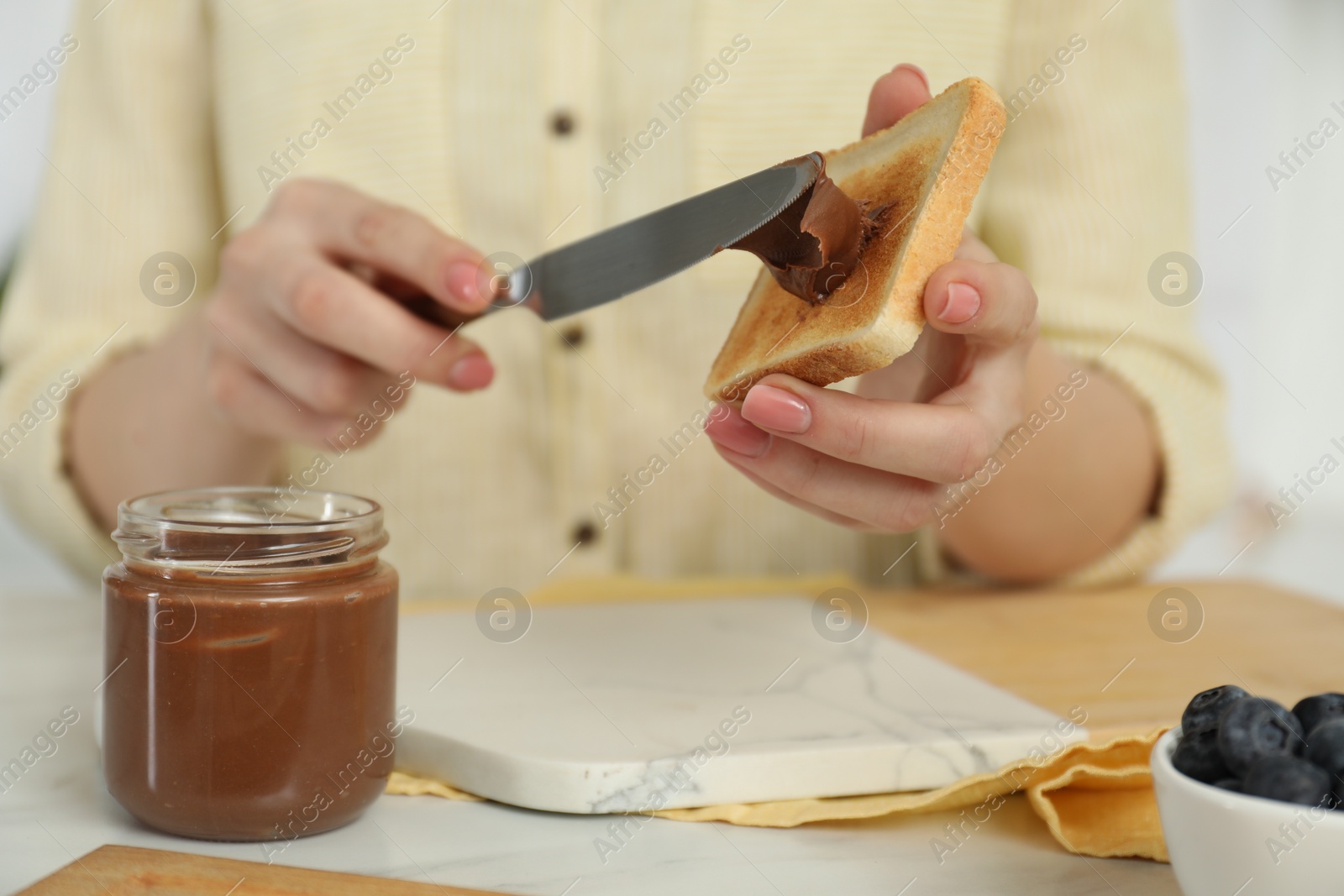 Photo of Woman spreading tasty nut butter onto toast at white table, closeup