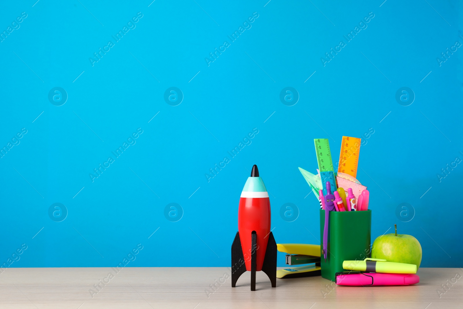 Photo of Bright toy rocket and school supplies on wooden desk. Space for text