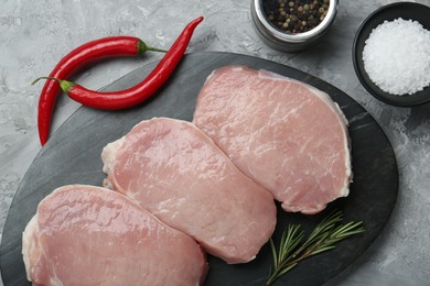 Photo of Pieces of raw pork meat, chili peppers and spices on grey textured table, flat lay