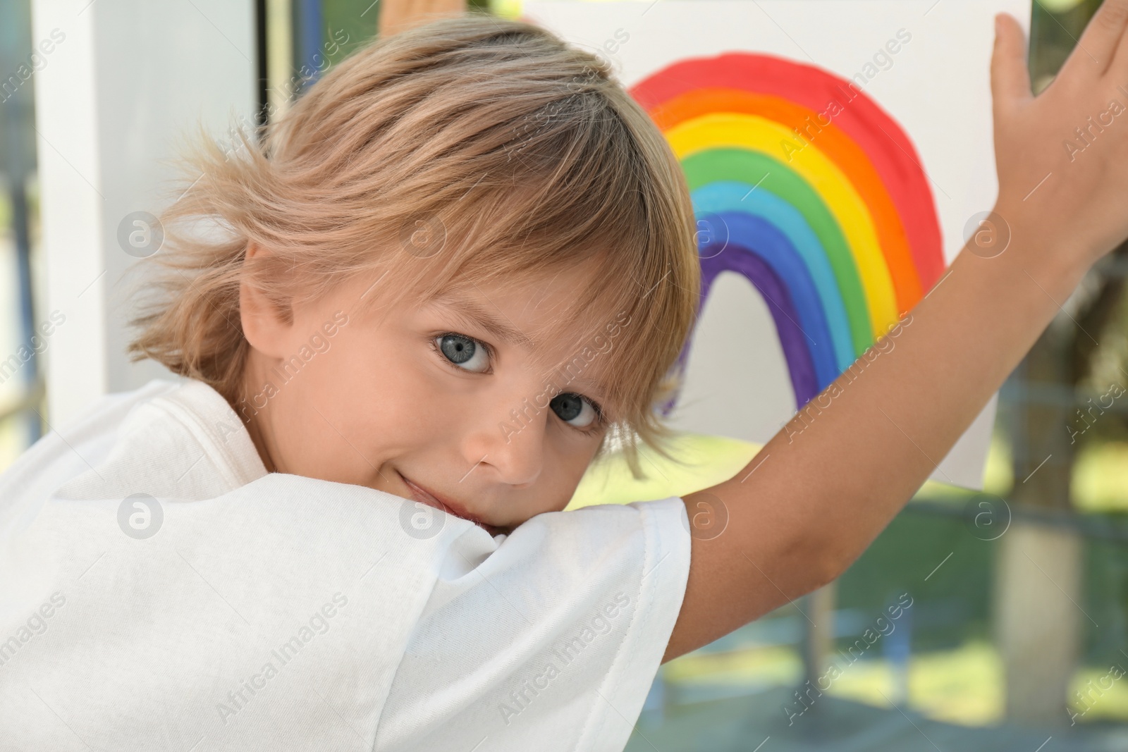 Photo of Little boy holding rainbow painting near window. Stay at home concept