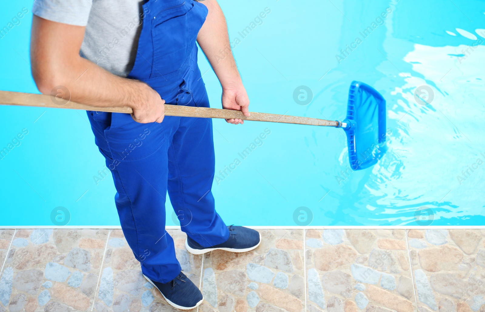 Photo of Male worker cleaning outdoor pool with scoop net