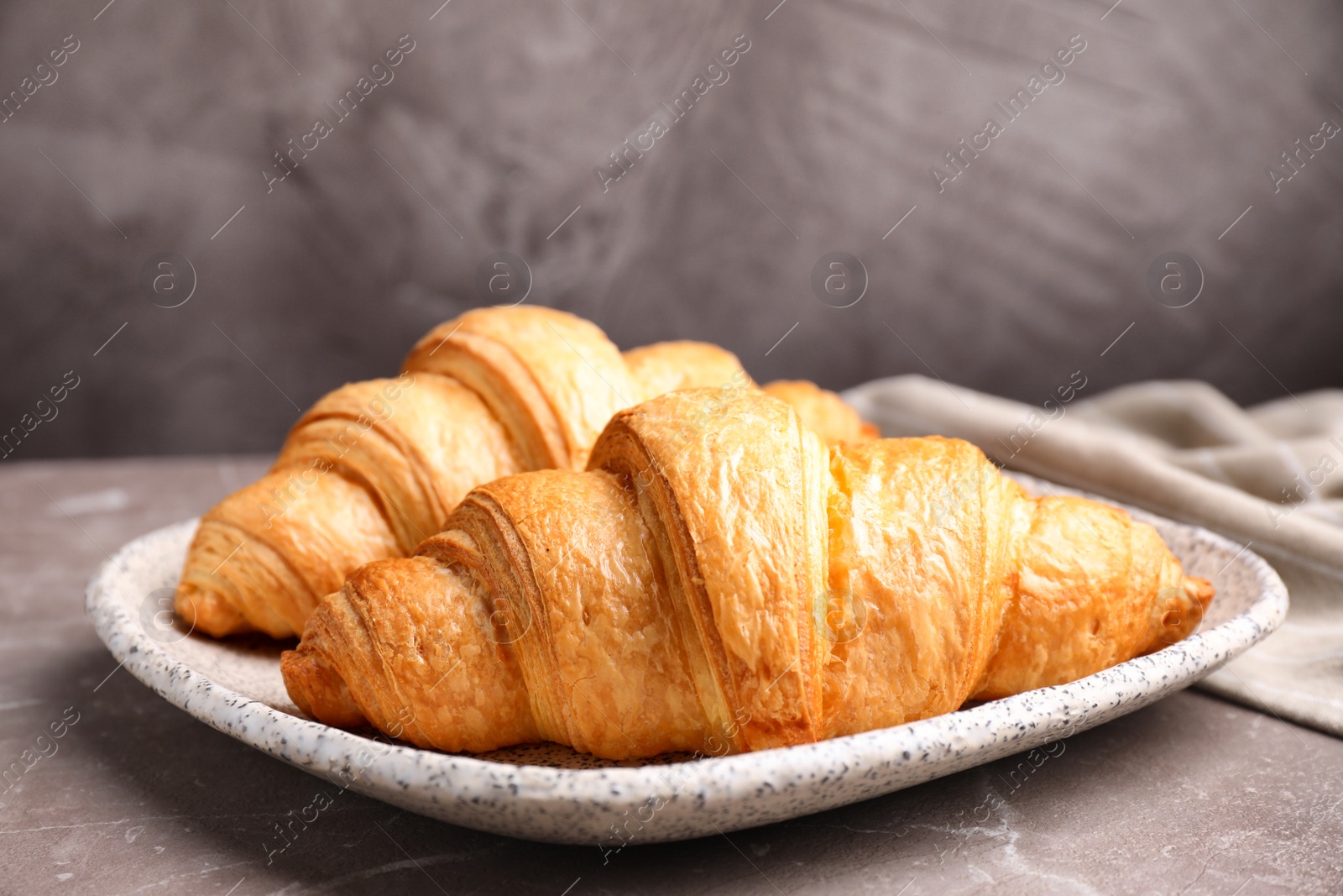 Photo of Tasty fresh croissants on brown marble table, closeup