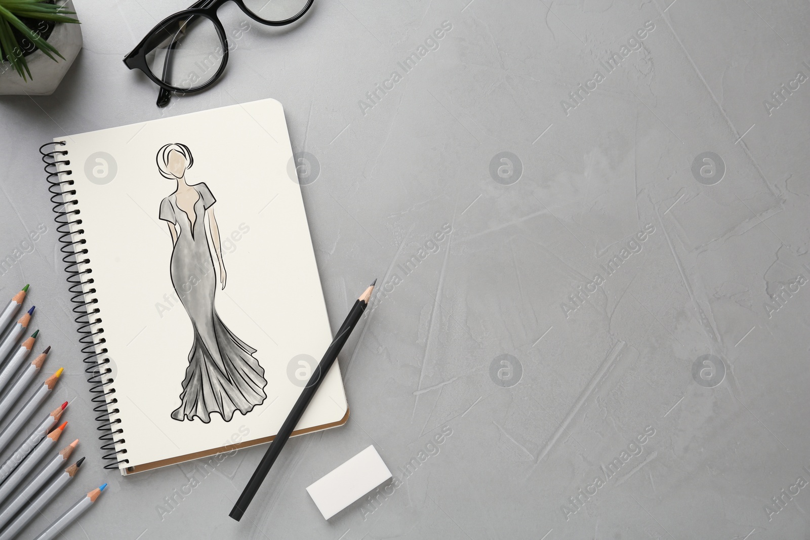 Image of Sketch of beautiful dress in pad on grey textured table, space for text. Fashion designer's desk with stationery, flat lay