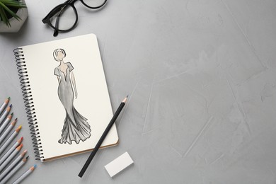 Sketch of beautiful dress in pad on grey textured table, space for text. Fashion designer's desk with stationery, flat lay