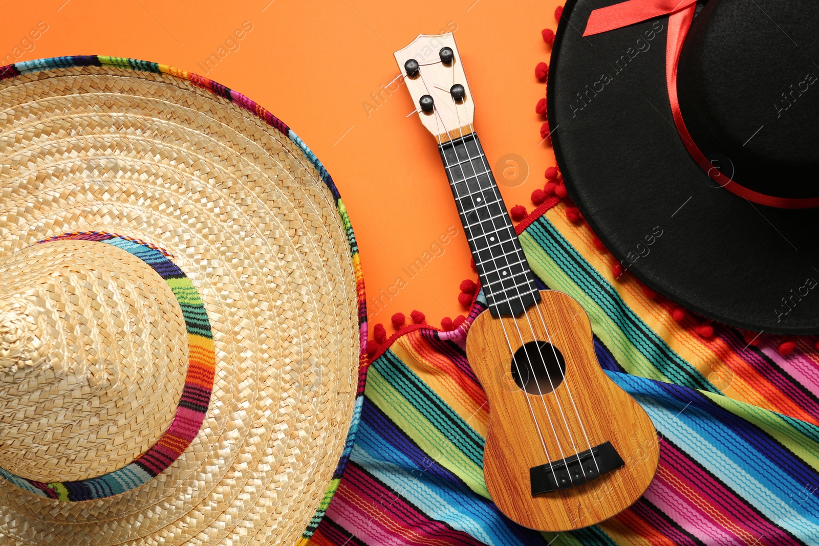 Photo of Mexican sombrero hats, guitar and colorful poncho on orange background, flat lay
