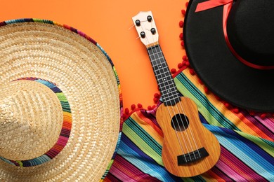 Mexican sombrero hats, guitar and colorful poncho on orange background, flat lay