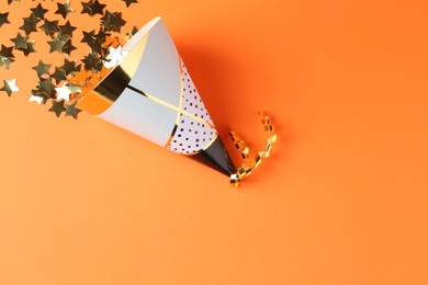 Photo of Party hat and confetti on orange background, top view. Space for text