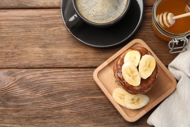 Plate of banana pancakes and honey served on wooden table, flat lay. Space for text