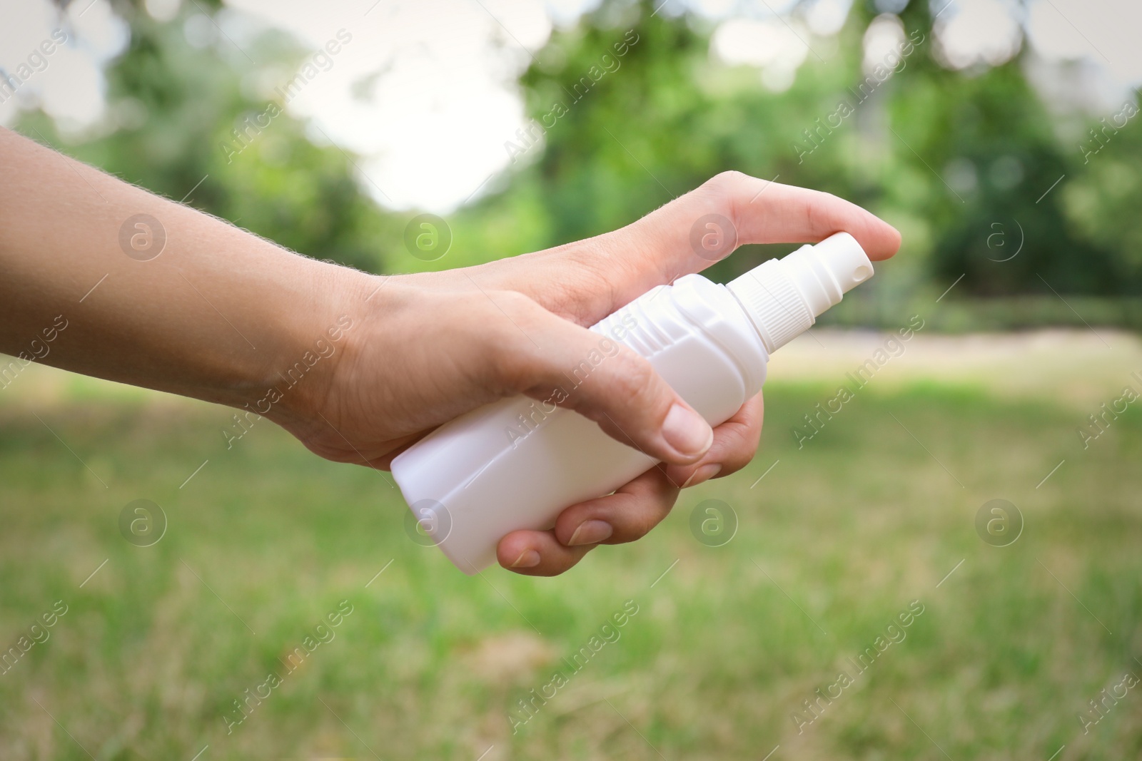 Photo of Woman with bottle of insect repellent spray outdoors, closeup