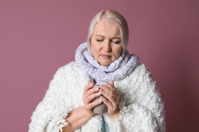 Mature woman with cup of hot tea suffering from cold on color background