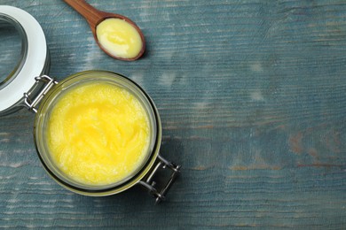 Photo of Glass jar and spoon of Ghee butter on light blue wooden table, flat lay. Space for text