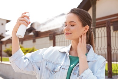 Young woman applying thermal water on face outdoors. Cosmetic product