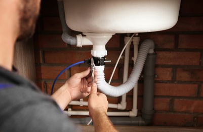 Photo of Professional plumber fixing sink drain, closeup of hands