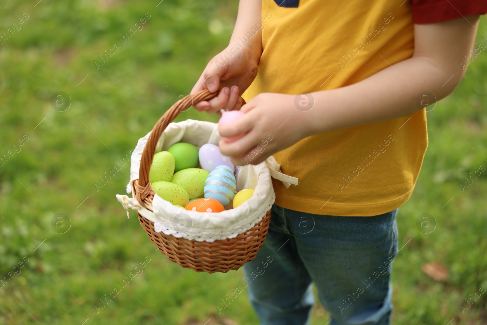 Photo of Easter celebration. Little boy holding basket with painted eggs outdoors, closeup