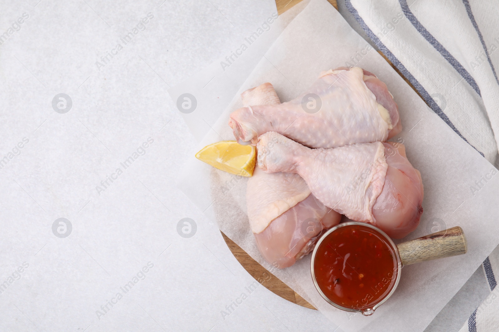 Photo of Fresh marinade, raw chicken drumsticks and lemon wedge on light table, top view. Space for text