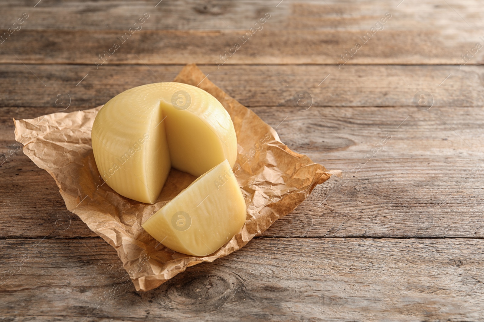 Photo of Parchment paper with cut wheel of delicious cheese on wooden table. Space for text