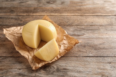 Parchment paper with cut wheel of delicious cheese on wooden table. Space for text