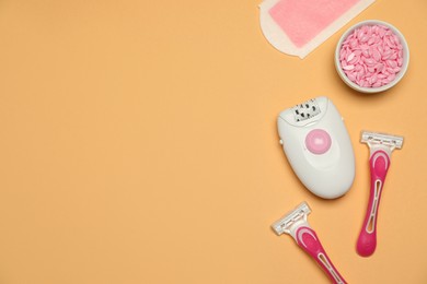 Photo of Modern epilator and other hair removal products on orange background, flat lay. Space for text