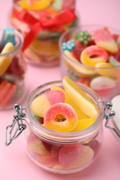 Photo of Glass jars with tasty colorful jelly candies on pink background, closeup