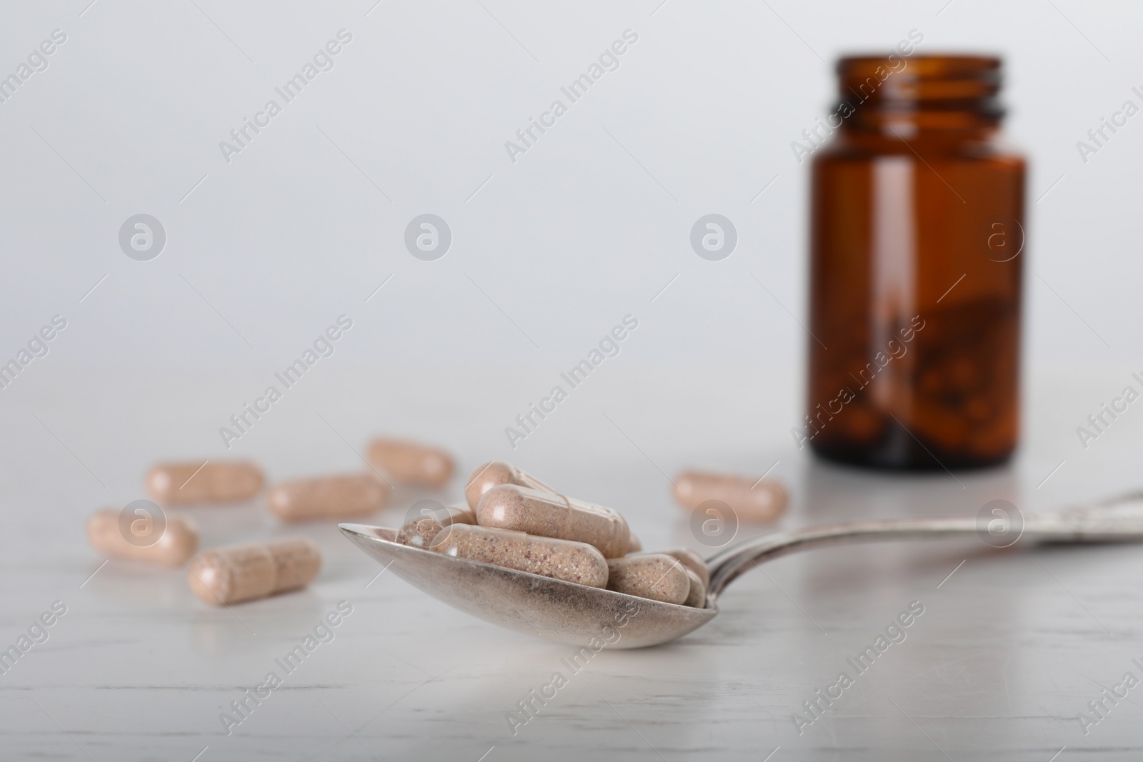 Photo of Gelatin capsules, spoon and bottle on white wooden table, closeup. Space for text